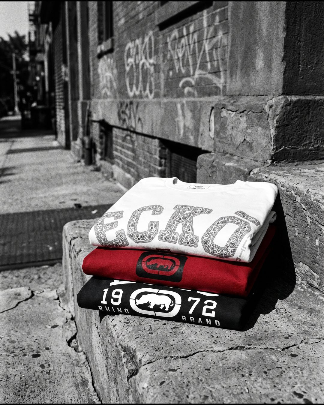 Three folded Ecko Unltd tees on a concrete stoop
